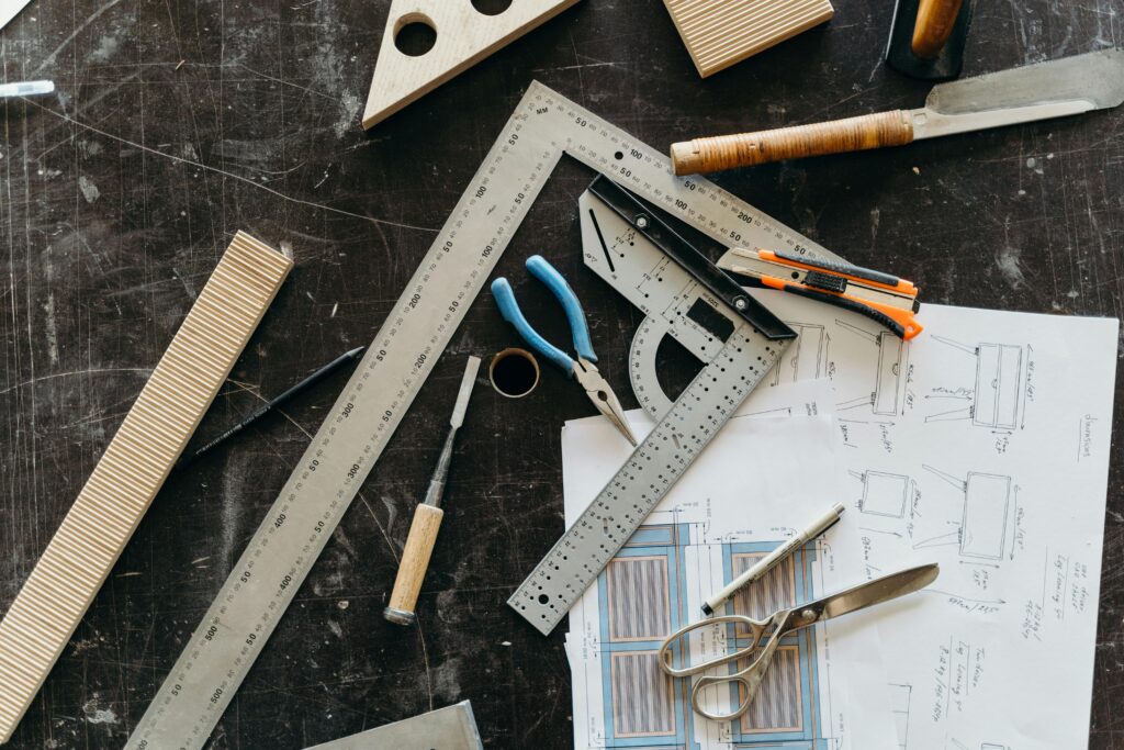 Top view of carpentry tools, design plans and sketching equipment on a brown surface.
